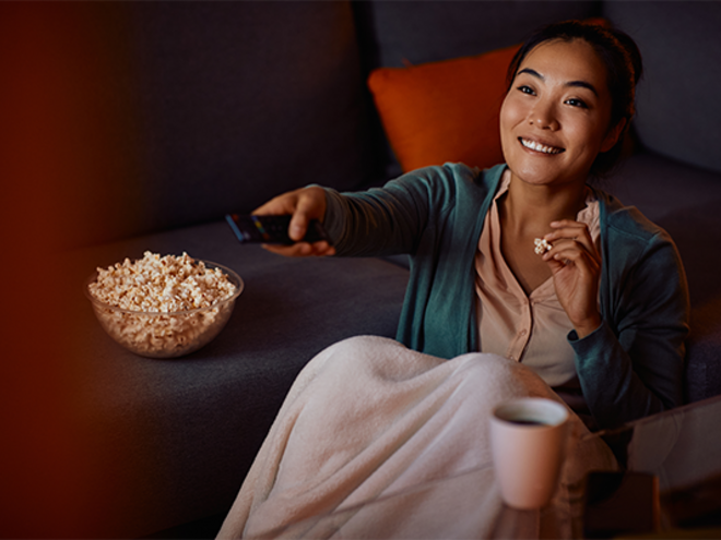 A young Asian mom relaxing on the sofa with a bowl of snacks, watching mom movies