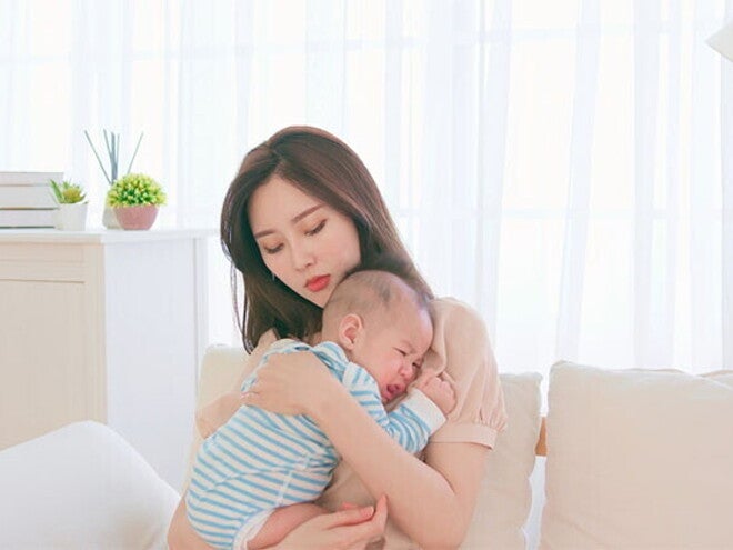 A young Asian mother carrying and soothing her baby on the sofa, worrying about colds in newborns. A young Asian mother carrying and soothing her baby on the sofa, worrying about colds in newborns.