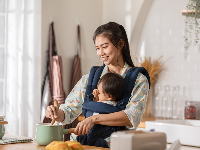 A young Asian woman carrying her baby and cooking food to ensure she gets vitamins for breastfeeding moms. A young Asian woman carrying her baby and cooking food to ensure she gets vitamins for breastfeeding moms.