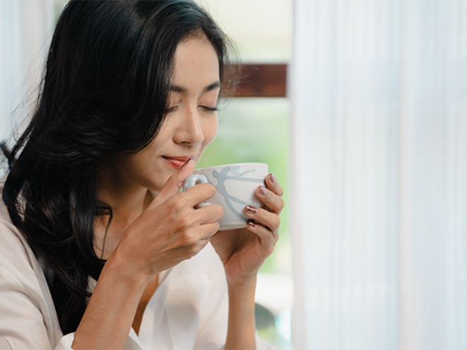 A young Asian woman enjoys a cup of coffee beside the window as part of her morning routine