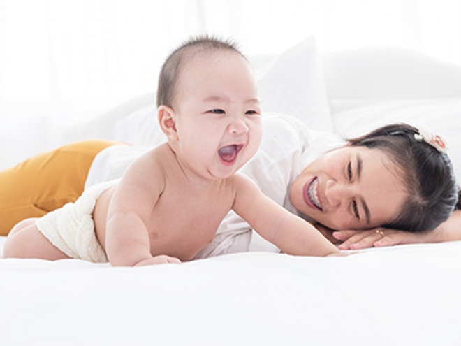 An Asian mother watching her smiling 6-month-old baby trying to crawl on the bed An Asian mother watching her smiling 6-month-old baby trying to crawl on the bed
