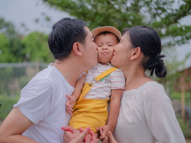  With physical touch as their son's love language, Asian toddlers gets a kiss on both cheeks from his Asian parents. 