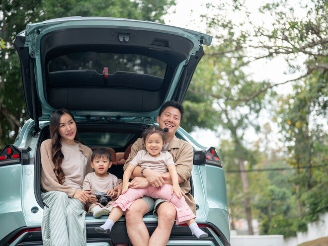 A happy Asian family sitting in the trunk of their car, enjoying a pit stop on their road trip.
