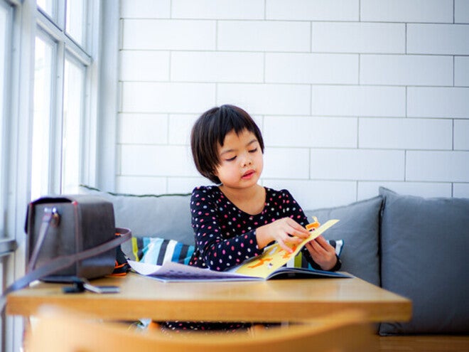 Asian little girl playing with a sticker book, one of her visual learning tools.
