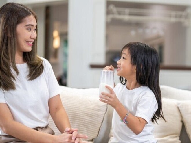 An Asian mom smiling at her daughter holding a glass of milk for the benefits of milk.