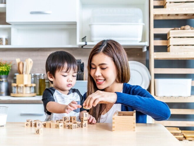 A young Asian mother and her little son stack wooden blocks to boost brain development.