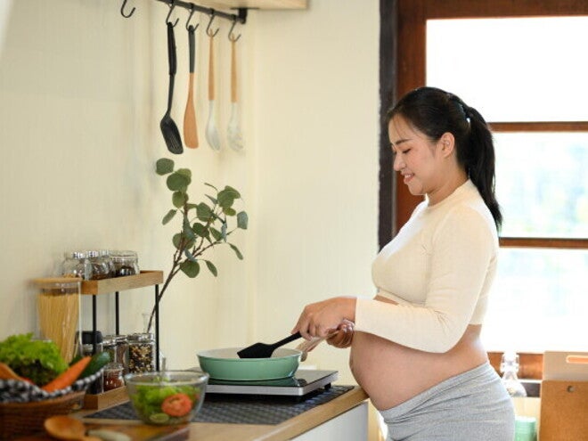 An pregnant Asian woman cooking food for pregnant women at home in her kitchen.