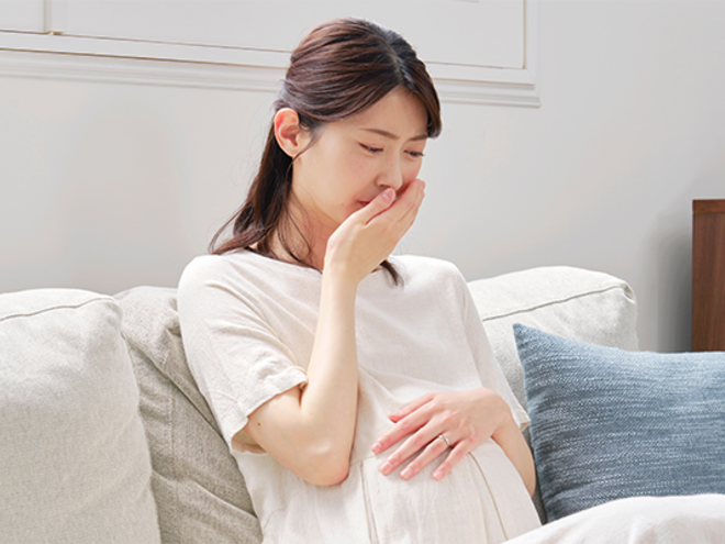Photo of a pregnant Asian woman with her hand to her mouth, experiencing acid reflux in pregnancy.