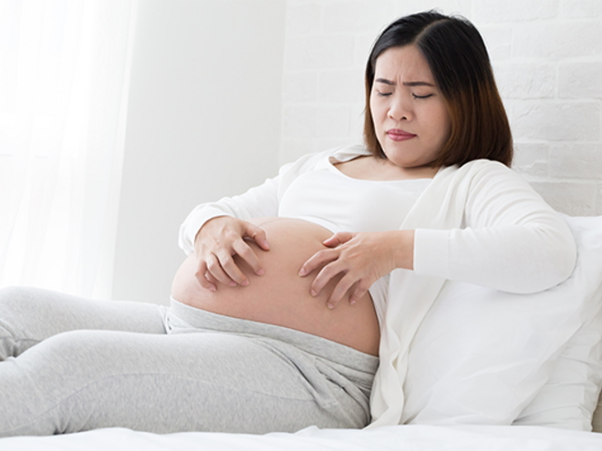Asian pregnant women scratching her belly as a symptom of a pregnancy rash.