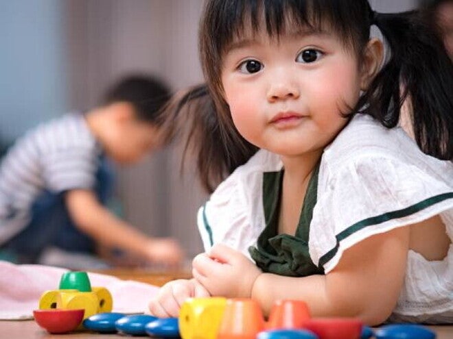 Asian 2-year-baby girl lies on her stomach on the floor while playing with her toys.