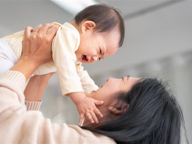 Asian baby girl grabs her mom's face as her mom lifts her Asian baby girl grabs her mom's face as her mom lifts her