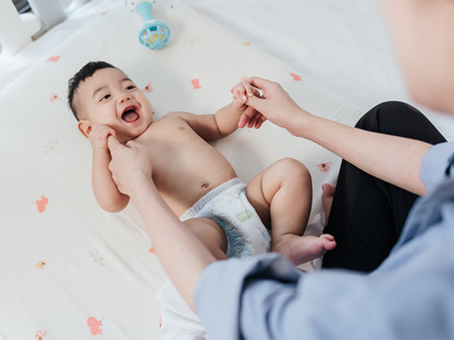 Asian baby laughs as his mom holds his hands during a baby massage.