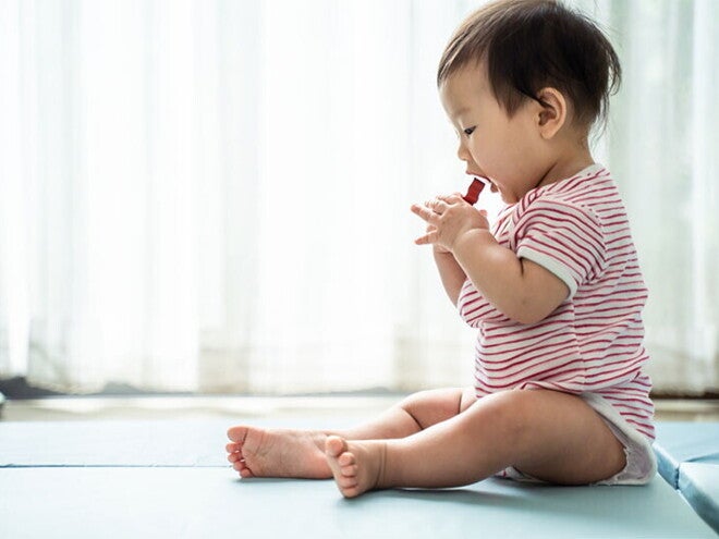 Asian baby sitting on a mat about to put a choking hazard in his mouth Asian baby sitting on a mat about to put a choking hazard in his mouth