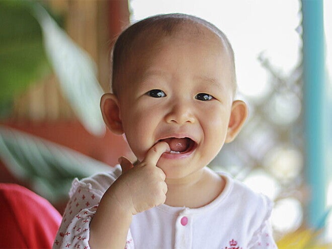 Asian baby with one of their fingers in their mouth.