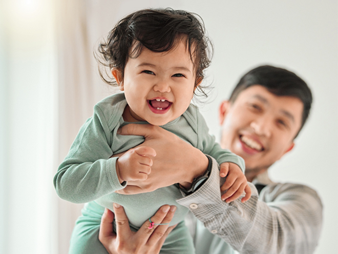 Asian dad lifts his laughing baby with both hands high in the air