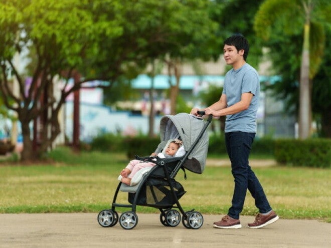 Asian dad pushes his baby's stroller through a park
