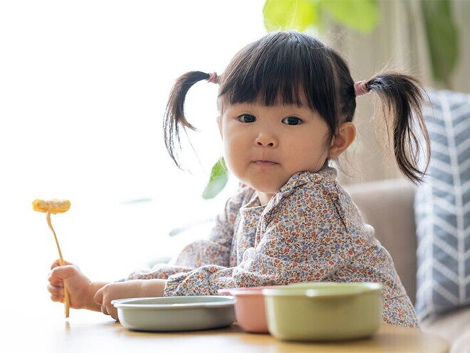 Asian female toddler prepares to eat as she holds her fork with food Asian female toddler prepares to eat as she holds her fork with food