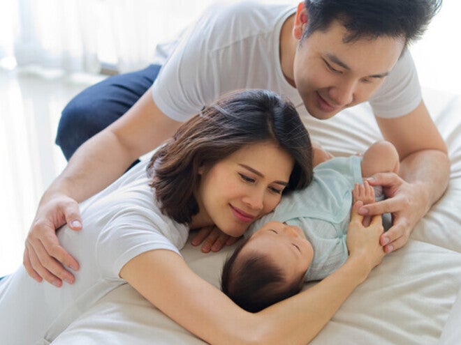 Asian mom and dad are hugging a newborn baby on the sofa at home
