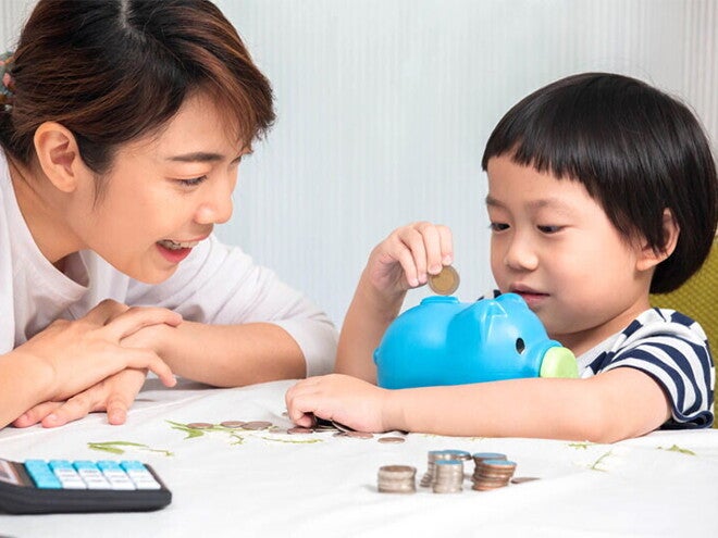 Asian mom and son putting coins in piggy bank