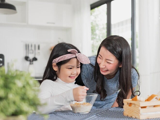 Asian mother watching her child eating cereal from a bowl Asian mother watching her child eating cereal from a bowl