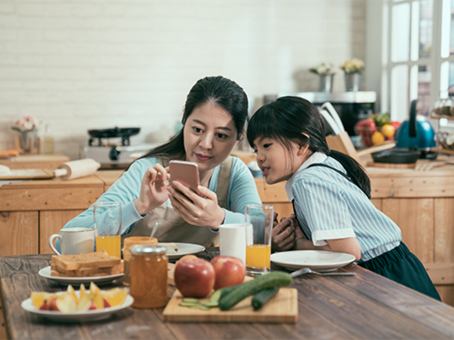 Asian mother with her daughter checking her smartphone at the kitchen table