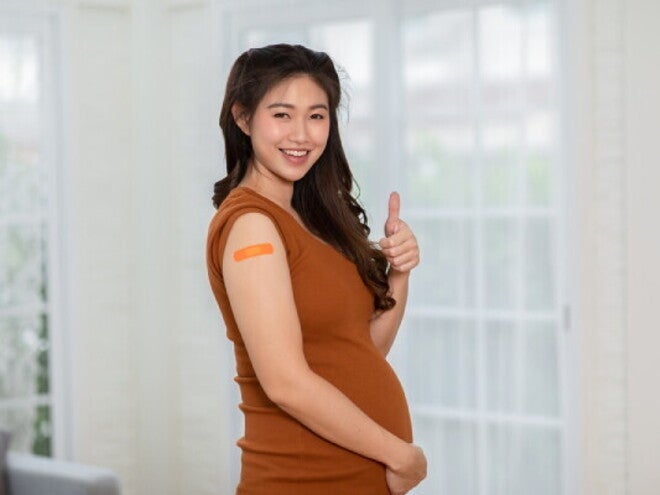 Asian pregnant woman performs a thumbs-up sign after getting vaccine for pregnant women.