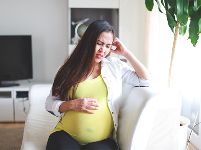 Asian pregnant woman winces in pain due to heartburn
