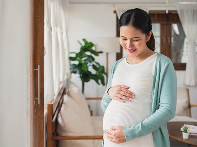 Asian woman at 27 weeks pregnant holds her baby bump