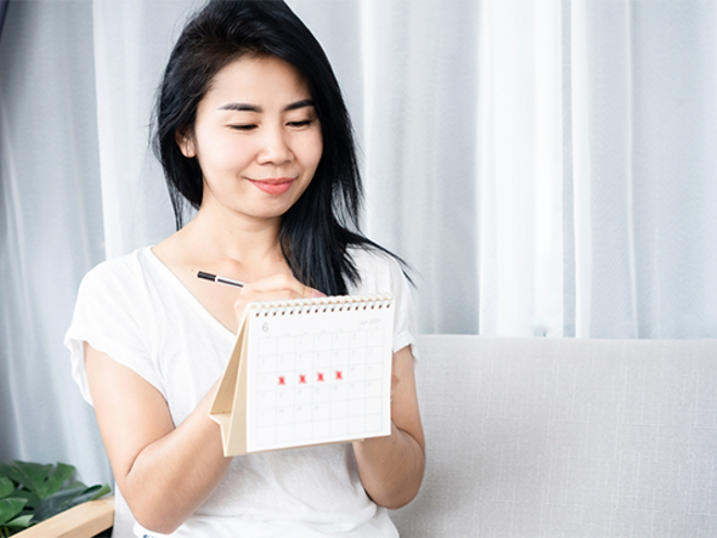 Asian woman checking the calendar for ovulation or menstruation to understand PMS symptoms vs pregnancy symptoms Asian woman checking the calendar for ovulation or menstruation to understand PMS symptoms vs pregnancy symptoms
