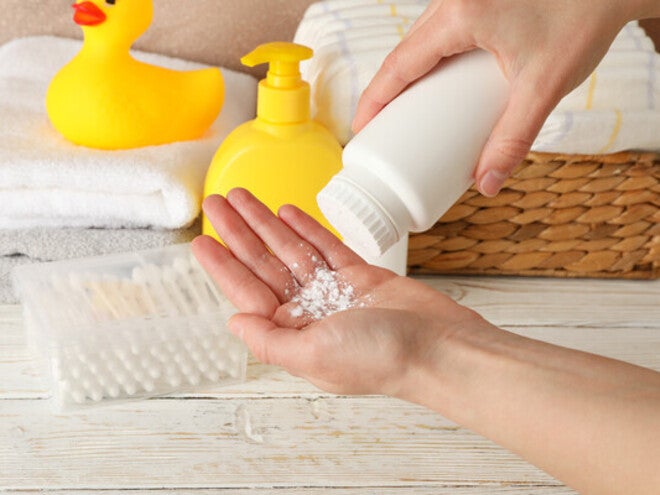 Close-up pic of one hand pouring baby powder onto the other hand, with towels and a yellow rubber duck in the background.