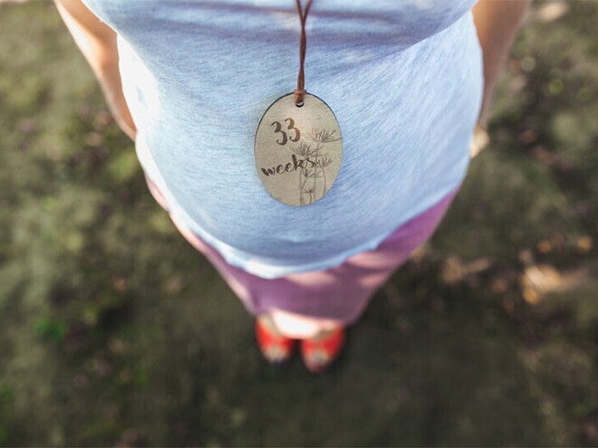 Cropped photo of pregnant Asian woman's belly wearing a necklace with a tag that says 33 weeks pregnant. 
