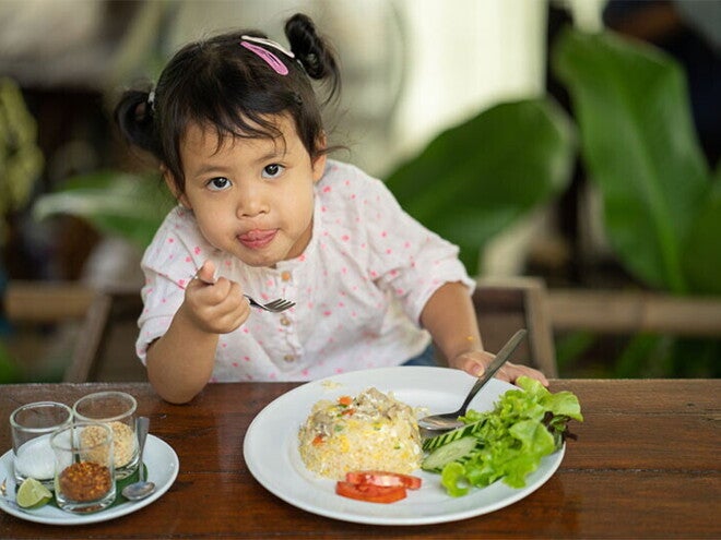 Cute Asian little girl eats fried rice with tomatoes and green leafy vegetables on the side Cute Asian little girl eats fried rice with tomatoes and green leafy vegetables on the side