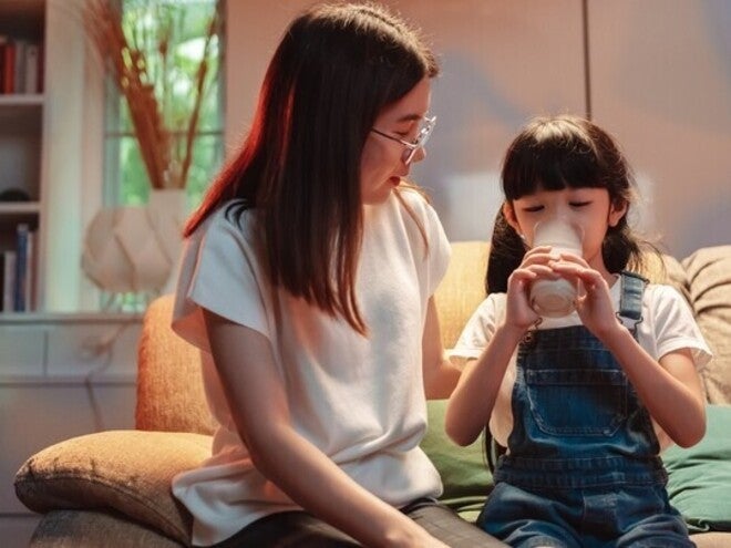 Asian mom watching her little girl drinking milk before bed, wondering does milk help you sleep?