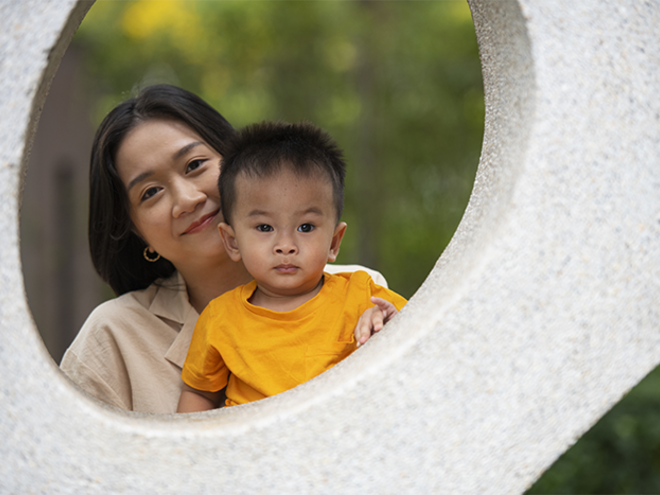  Mother and toddler child smiling together through a circular stone frame outdoors, close-up portrait with soft natural background, parenting, family bonding, and motherhood concept.