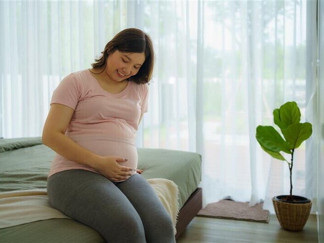 Happy pregnant Asian woman touches her pregnant belly while sitting on the bed. Happy pregnant Asian woman touches her pregnant belly while sitting on the bed.