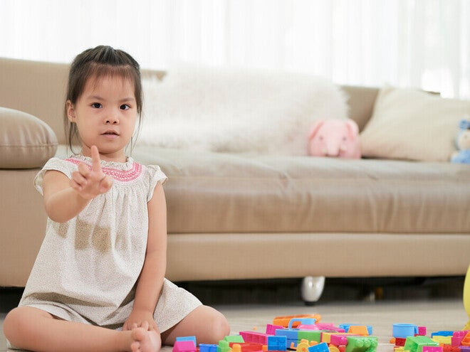 A little Asian girl sitting on the floor in living room, counting with her fingers, using math for kids.