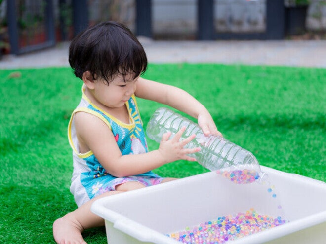 Little Asian boy playing with a DIY Montessori toy, like an empty plastic bottle and beads in a container