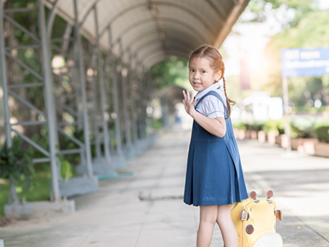 Little Asian girl going back to school with her backpack, waving