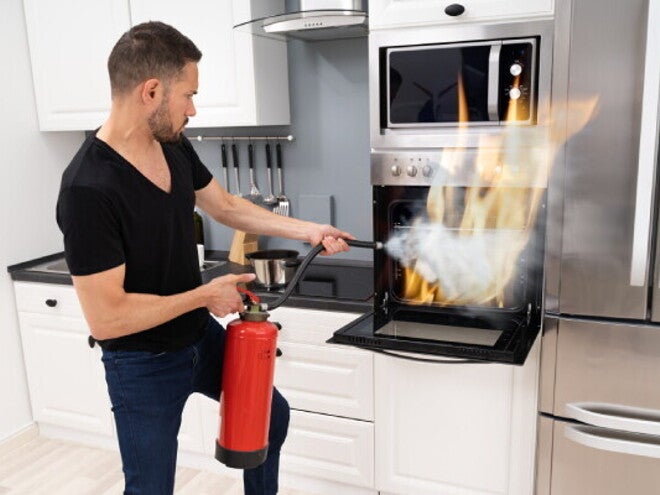 A young man using a fire extinguisher to put out a fire in an oven after learning fire safety tips. 
