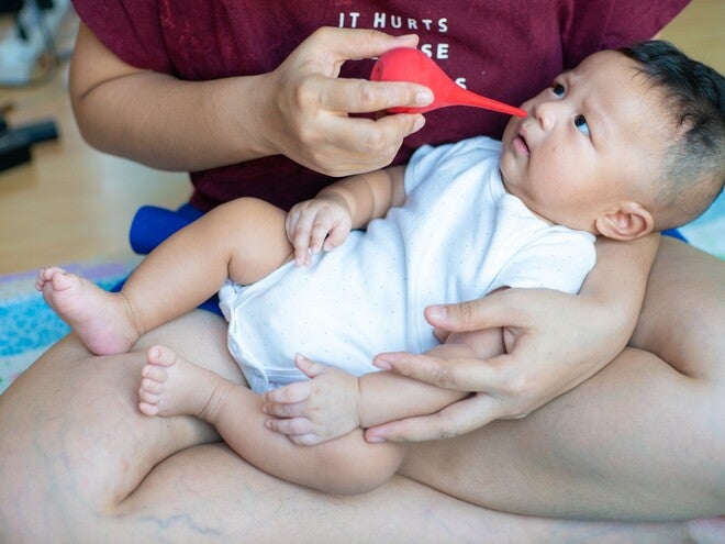 Cropped photo of a mom using a bulb syringe nasal aspirator to suck out snot from her baby’s nose.