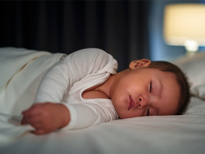 Newborn baby in a white onesie asleep in bed in the evening. Newborn baby in a white onesie asleep in bed in the evening.