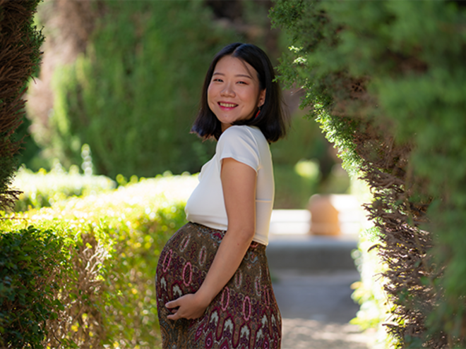 Smiling pregnant Asian woman wearing a cotton dress outdoors and showing off her baby bump.