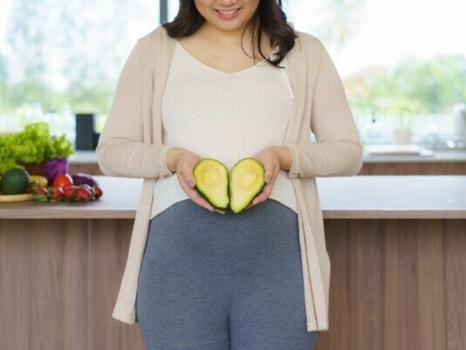 Pregnant Asian woman holding a sliced avocado—one of the best fruits for pregnant women