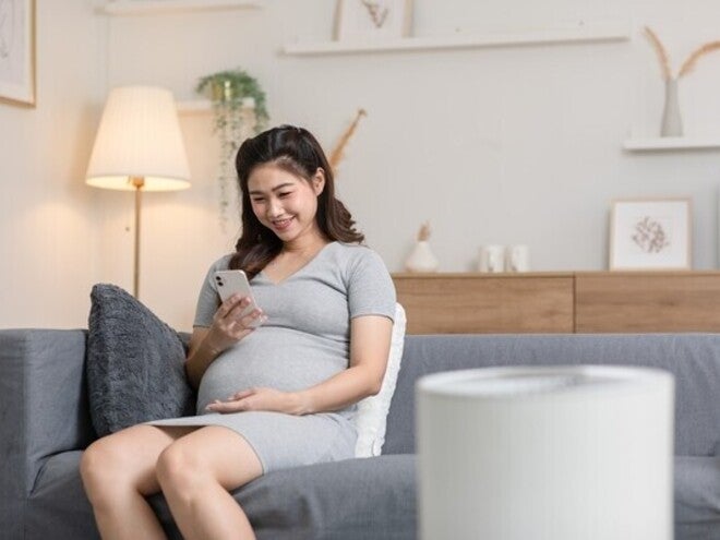 Pregnant Asian woman on a sofa looking at her pregnancy app on her phone at home