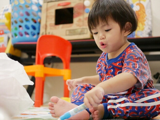 Asian 18-month-old baby scribbles with a pen during playtime.