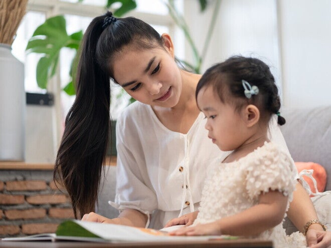 A young Asian mother and her daughter reading a Filipino children’s book together. 