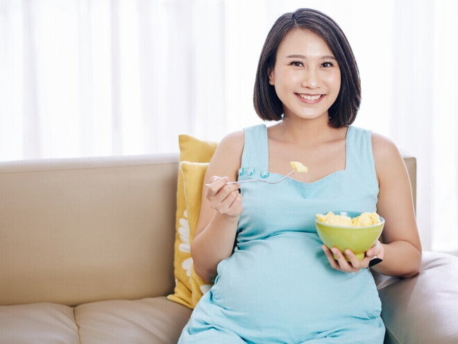 Header_Image Young and smiling Asian pregnant woman eat a bowl of fruits good for pregnancy.
