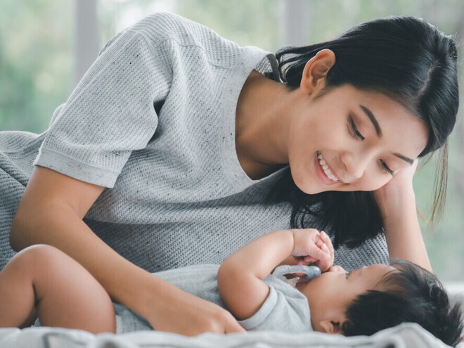 Header_Image Young Filipino mom smiles down at her baby as she lies down beside them.