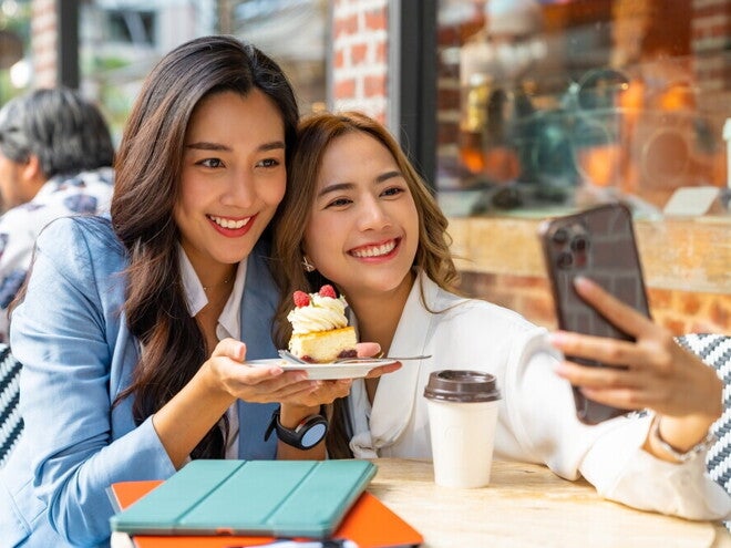 Header_Image Two Asian working moms take a selfie after meeting for dessert during lunch break.