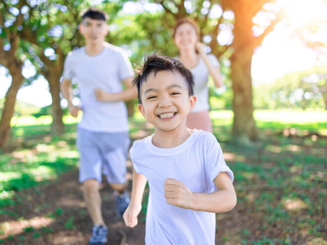 Happy healthy Asian boy running in the park with his parents behind him